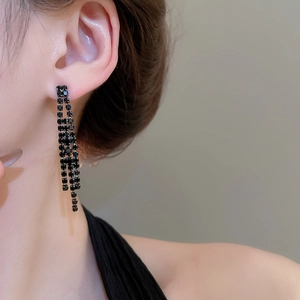 Gros plan sur des boucles d'oreilles à pompons noirs et strass portées par un mannequin