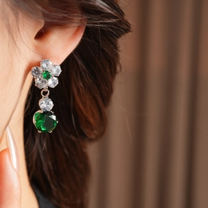 Detailed close-up of zircon flower earrings with a pear-cut green emerald-style gemstone