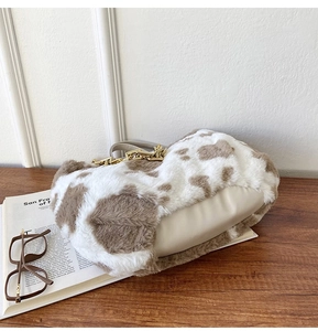 Detailed view of plush cow print tote bag with gold chain strap on wooden table