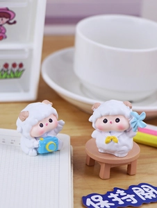 Detail of two mini lamb figurines holding a camera and fan on a wooden office desk