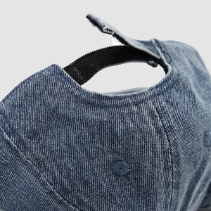 Detail of adjustable hook and loop strap on blue denim baby cap with ventilation holes
