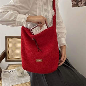 Primer plano de bolso tote de felpa roja con parche de cuero en silla de mimbre