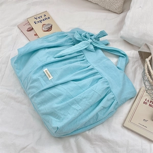 Close-up of light blue pleated canvas tote bag with bow detail on white bedding