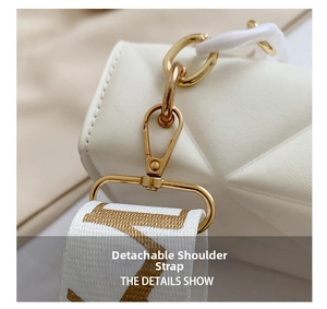 Close-up of white quilted crossbody bag with golden metal hook and lettered fabric strap