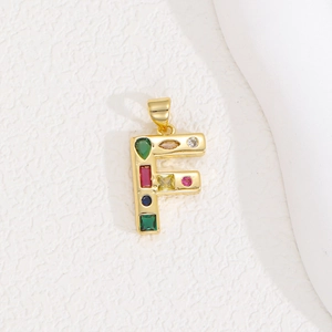 Macro detail of gold letter F pendant featuring colorful inlaid zircon gemstones