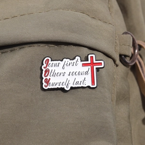 Macro d'un pin's Joy en émail avec croix rouge sur un sac à dos en toile kaki