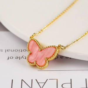 Macro shot of gold butterfly necklace pendant with pink enamel and beaded edge finish