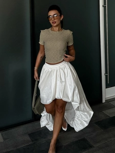 Détail d'une jupe blanche asymétrique en coton avec un haut olive texturé et un sac chic