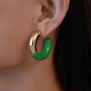 Detail of model wearing gold and green acrylic C-shaped hoop earrings with a glossy finish