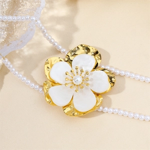 Detail view of a gold flower pendant with shell petals and pearls on a white necklace