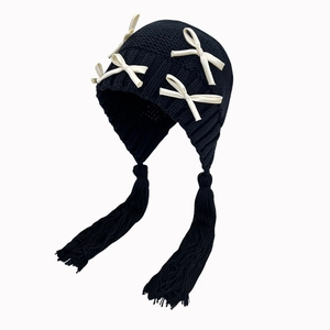 Detaillierte Ansicht einer schwarzen Strickmütze mit beigen Schleifen und Quasten.