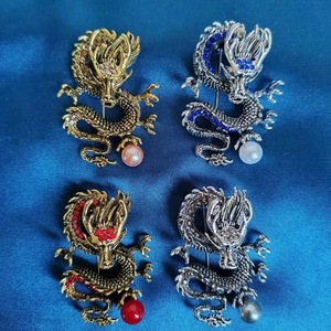 Detailaufnahme der Drachenbroschen mit bunten Strasssteinen auf blauem Seidenstoff