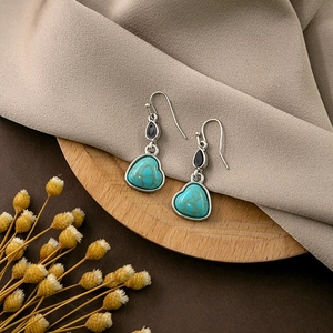 Detailed shot of heart-shaped turquoise pendant earrings resting on a wooden tray