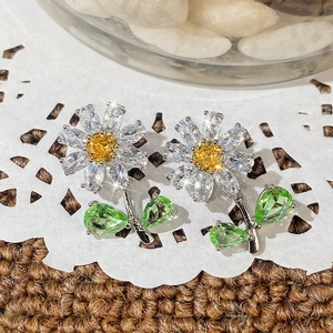 Close-up of daisy stud earrings with yellow centers and clear stone petals on lace