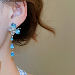 Detail of blue butterfly tassel earrings with cubic zirconia on model with soft lighting