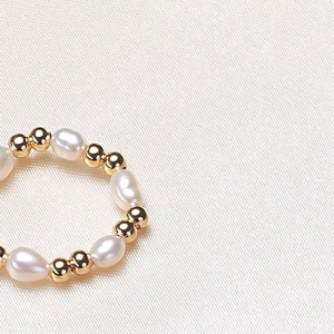 Elegant freshwater pearl and gold bead elastic ring on textured cream silk background