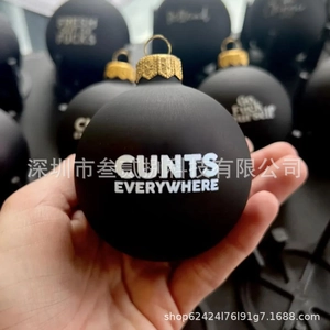 Close-up of a matte black Christmas ornament featuring bold white typography and gold hook
