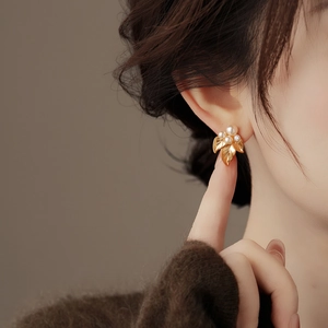 Close-up of elegant leaf-shaped gold stud earrings with white pearls and small zircon stones