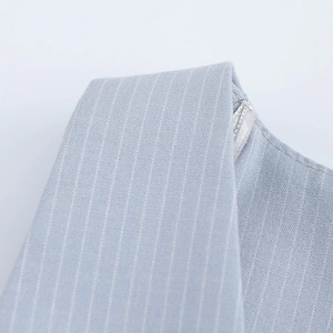 Dettaglio del gilet a righe azzurre con scollo a V e finiture metalliche argentate