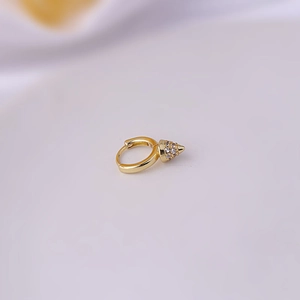 Macro detail of a golden cone earring with white zircon stones on a soft background