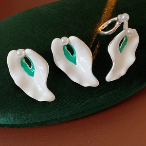 Detailed macro view of white enamel flower petal earrings with pearls on green velvet fabric