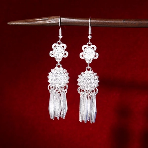 Detailed view of silver flower earrings with long tassels on a dark wood stand