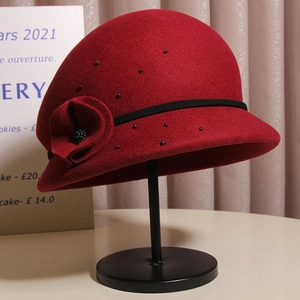 Dettaglio cappello cloche in lana rosso scuro con fiore e perle su supporto metallo