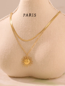 Detailed close-up of double-layered gold sun pendant necklace on a beige display mannequin