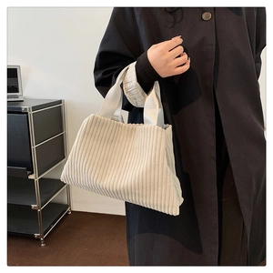 Detail of a beige corduroy bucket bag being carried by a model in a black wool coat