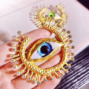 Detailed view of a gold Evil Eye brooch with radiant beams and blue rhinestone iris detail