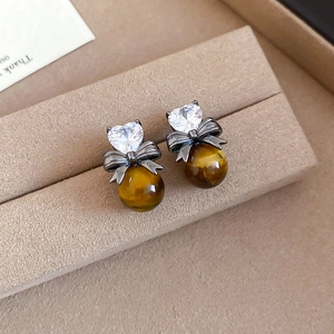 Detail of tiger eye earrings with heart zircon and black bow on beige velvet