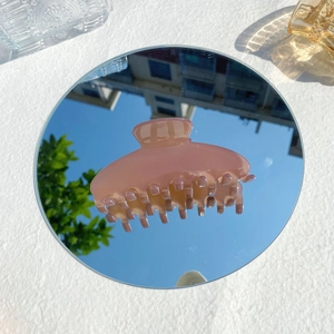 Close-up of a glossy pink hair claw clip reflecting clear blue sky on a mirror surface