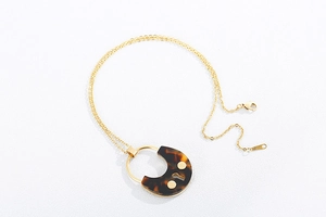 Detail of a gold-plated necklace featuring a tortoiseshell texture round pendant and clasp