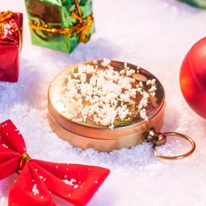 Close-up of golden brass compass with hanging ring on festive snow and gift background