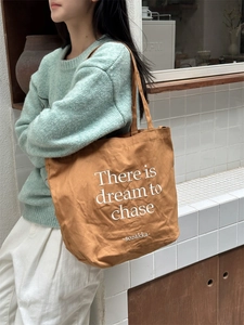 Caramel brown canvas tote bag with letter print shown on model in a minimalist lifestyle setting
