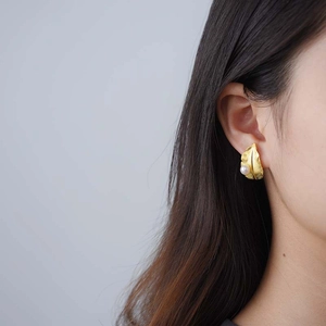 Golden leaf stud earrings with white pearl detail for women on model ear lobe