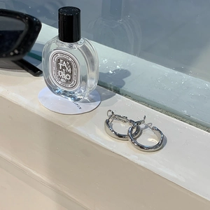Silver round hoop earrings on a windowsill with perfume and sunglasses for a stylish lifestyle