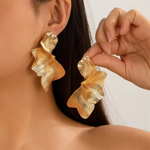 Gold oversized leaf irregular petal earrings worn by a model in a stylish studio setting
