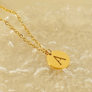 Macro detail of gold-plated titanium necklace with letter A engraved on a round pendant