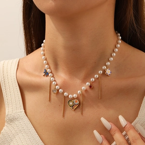 Dettaglio collana di perle con ciondoli a cuore e farfalla dorati indossata da modella