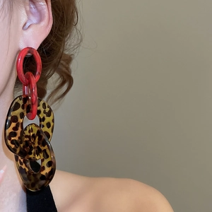 Close-up of leopard print acrylic chain earrings with red accents on a model