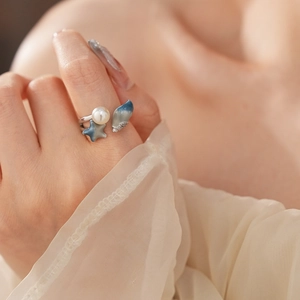 Macro detail of silver open ring with blue starfish shell and pearl on finger