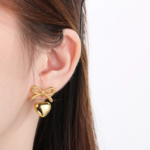 Close-up of elegant gold bow and heart stud earrings worn to show the polished texture