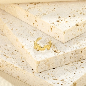 Macro detail of gold plated geometric leaf ear cuff on beige travertine stone display