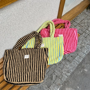 Détails de trois sacs cabas rayés en peluche colorée posés sur un banc en bois extérieur