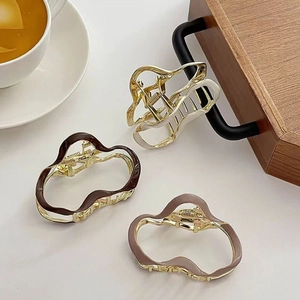 Three wavy metal hair claws in coffee, lavender, and cream finish on a wooden tray