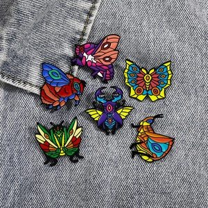 Colorful enamel insect pins including butterfly and beetle on blue denim fabric