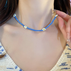 Detail view of blue beaded necklace with white daisy accents on neck for summer styling