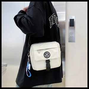 Close-up of white canvas crossbody bag with black buckle and astronaut pendant charm