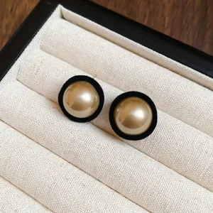 Elegant gold faux pearl earrings with black velvet trim on a rustic jewelry box